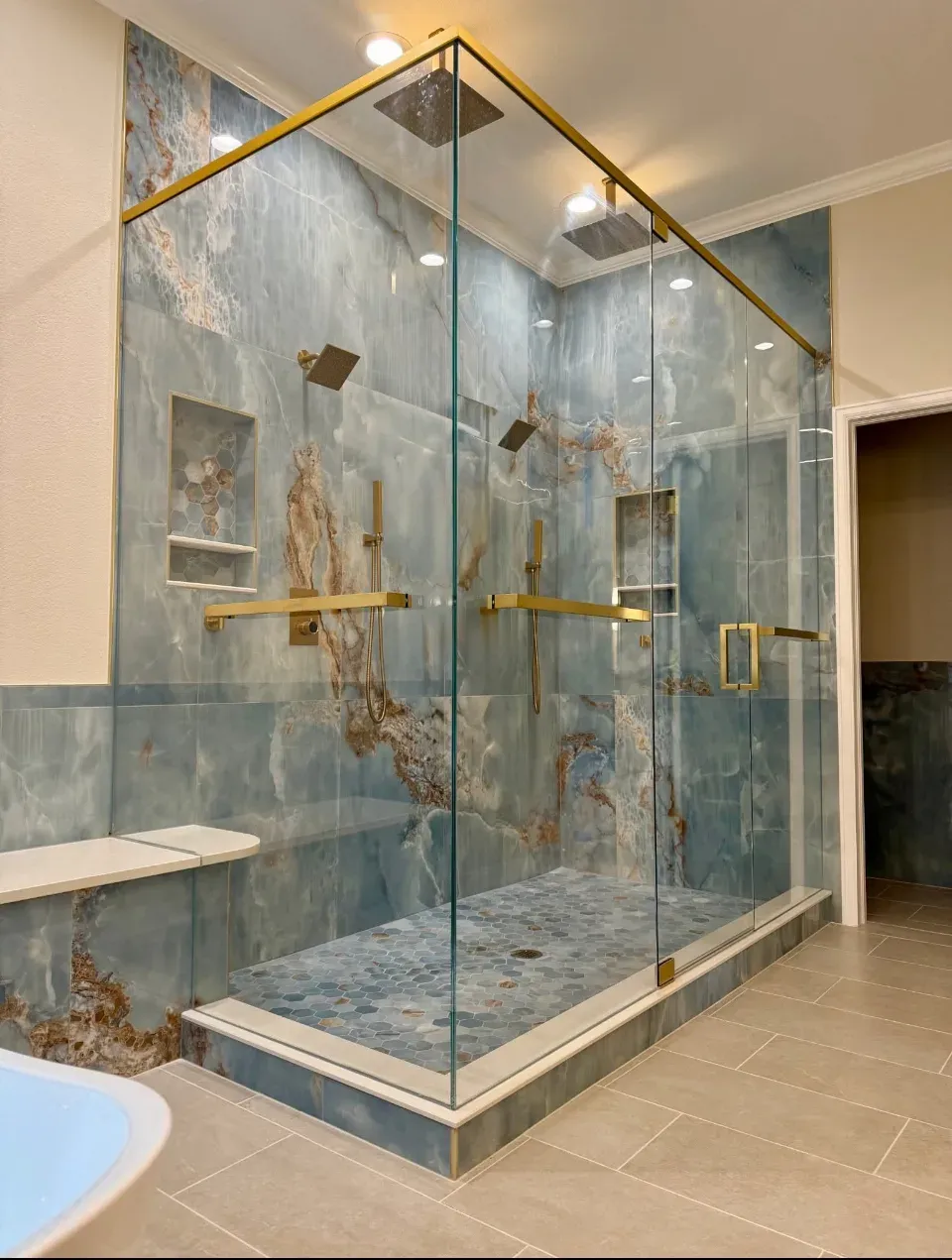 Completed bathroom: frameless glass shower with brass details and blue onyx-look porcelain tile